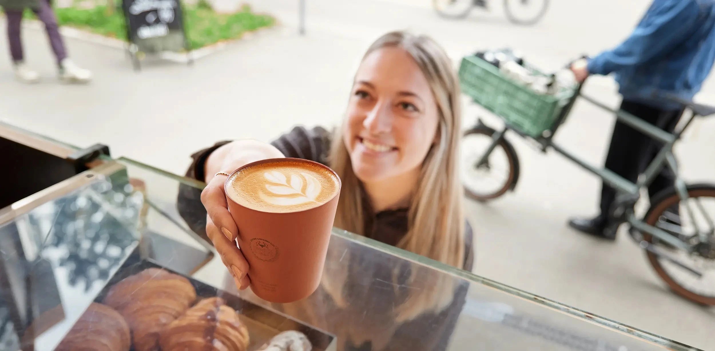 Barista serviert Cappuccino mit Latte Art im ViCAFE Espresso Bar Fenster in Zürich – Spezialitätenkaffee aus frisch gerösteten Kaffeebohnen
