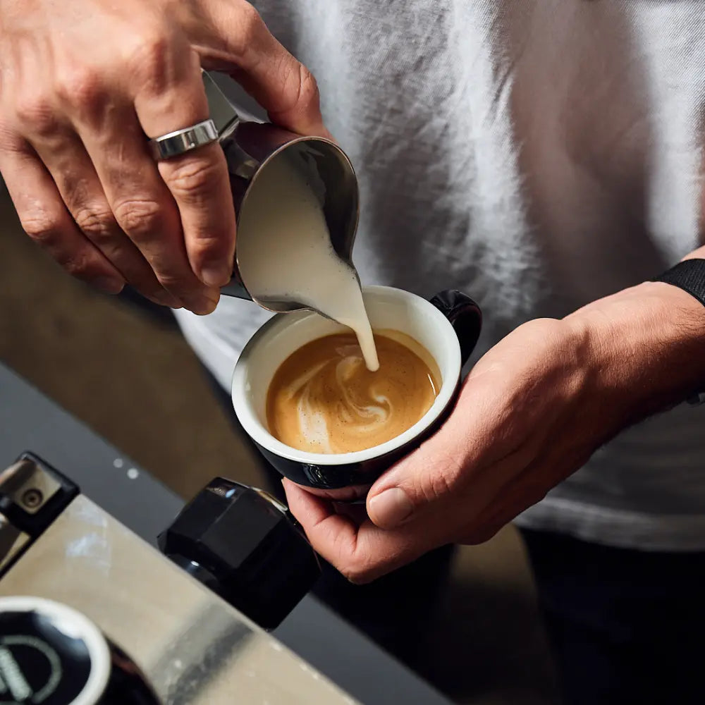 Milch wird in einen frisch gebrühten Espresso gegossen – Latte Art als Inspiration für perfekten Kaffeegenuss zuhause mit ViCAFE.