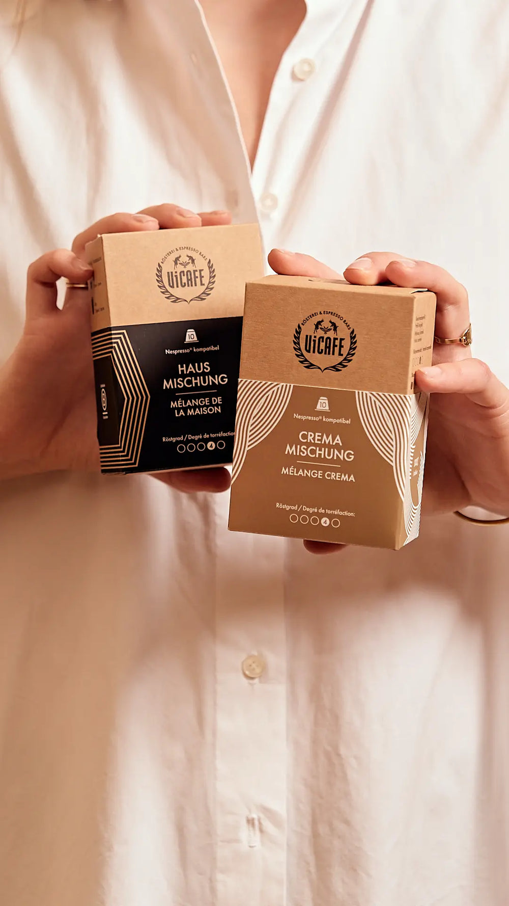Two hands holding two boxes of ViCAFE Specialty Coffee Capsules against a neutral background