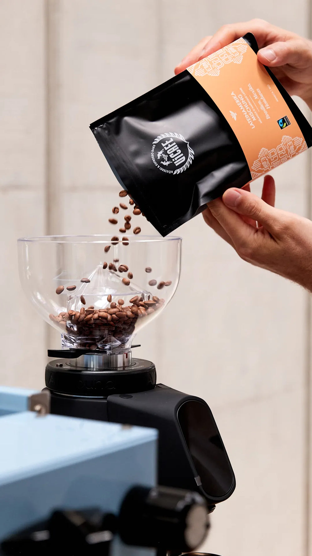 Hand pouring freshly roasted coffee beans from a bag into a grinder at home